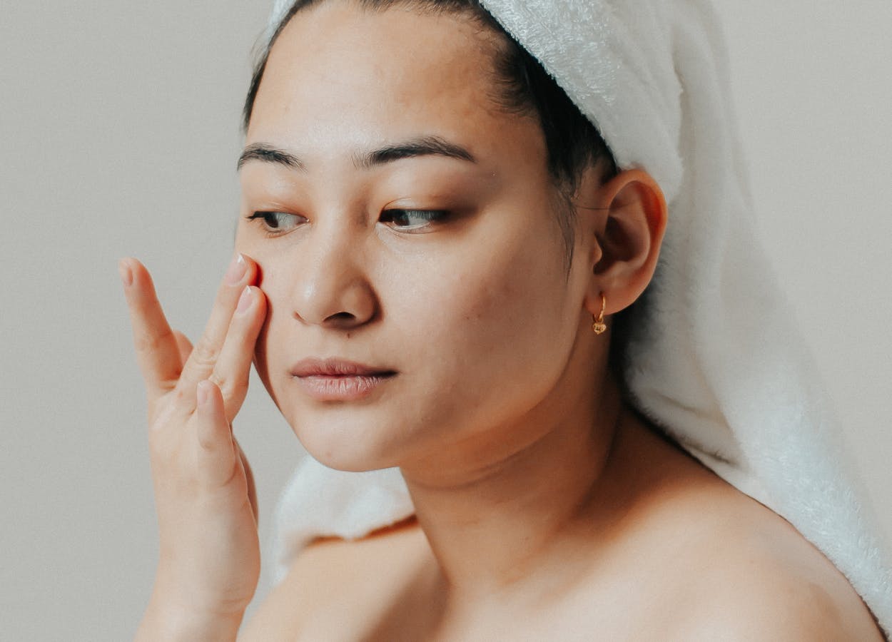 A woman touches her face as she applies skincare