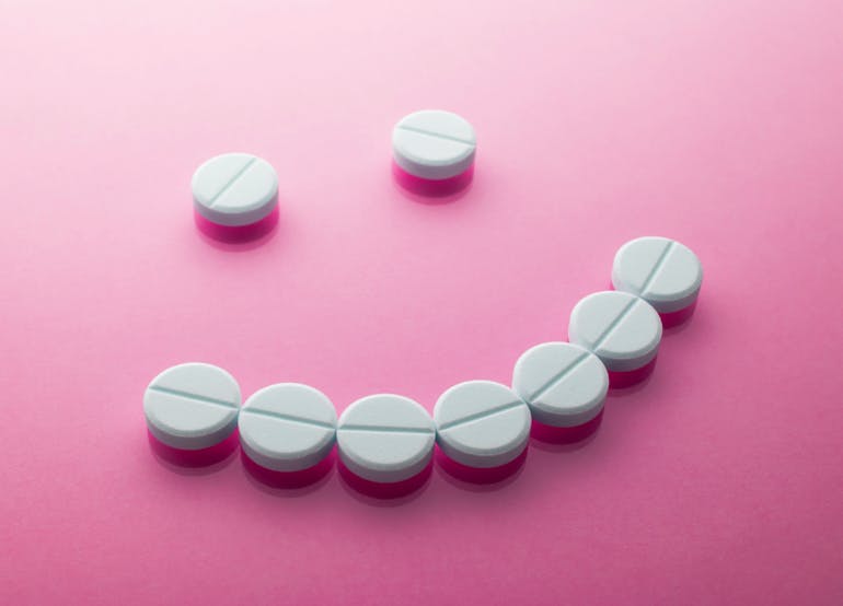 White pain relief tablets in the shape of a smiley face on a pink background