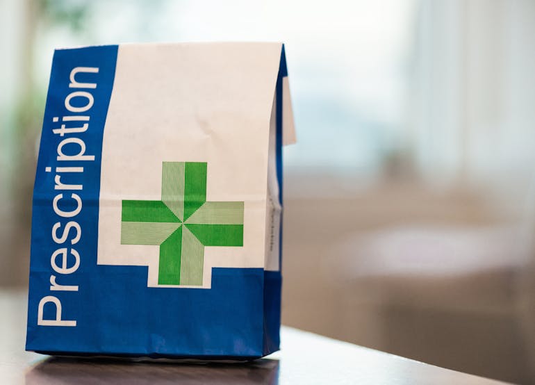 White and blue paper bag with a green cross, with the word 'Prescription' printed on