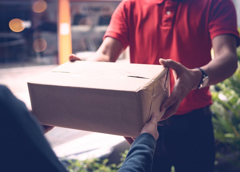 A delivery worker hands over a boxed package to outreached hands