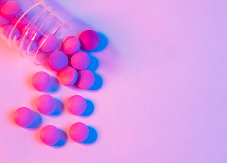 Clear bottle of pink pills spilling out onto a pink background