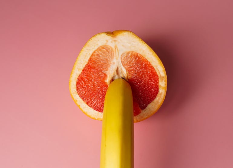 Image of banana poking into a half cut orange on a pink background