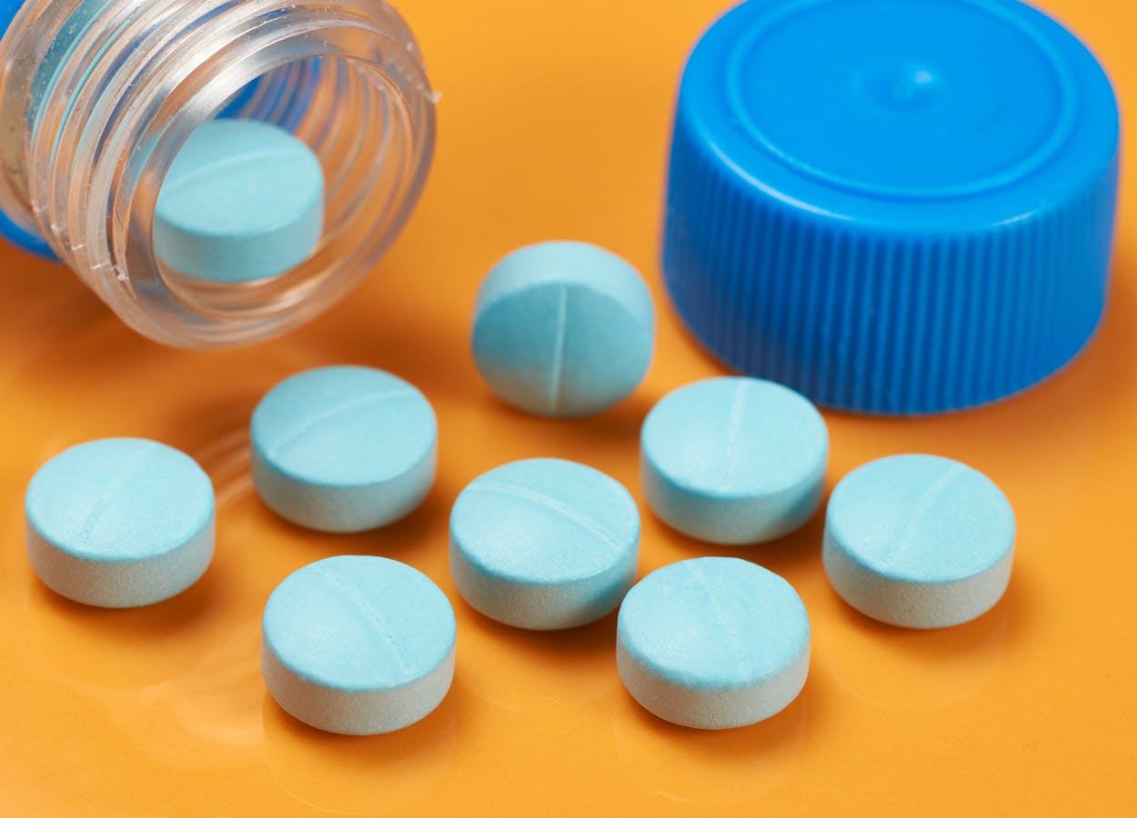 Blue round tablets spill out of a bottle onto an orangle surface