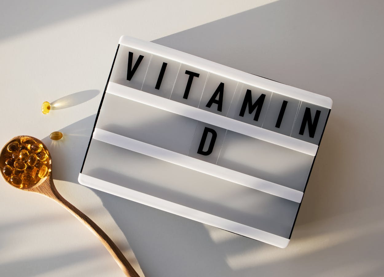 Pill capsules in a spoon next to a baord with text saying: 'Vitamin D'